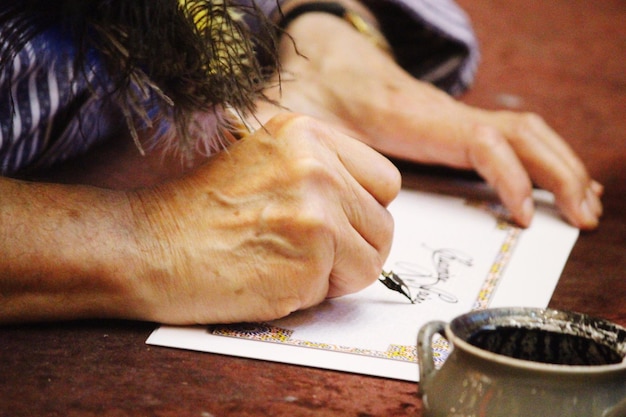 Image coupée d'une femme écrivant sur papier avec un stylo plume sur la table