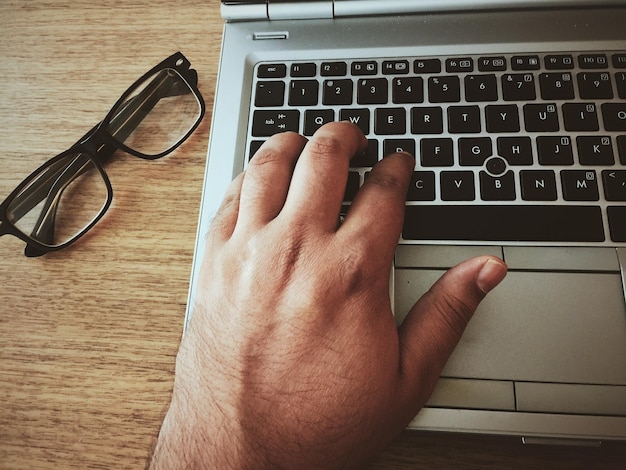 Image coupée d'un homme utilisant un ordinateur portable avec des lunettes sur la table