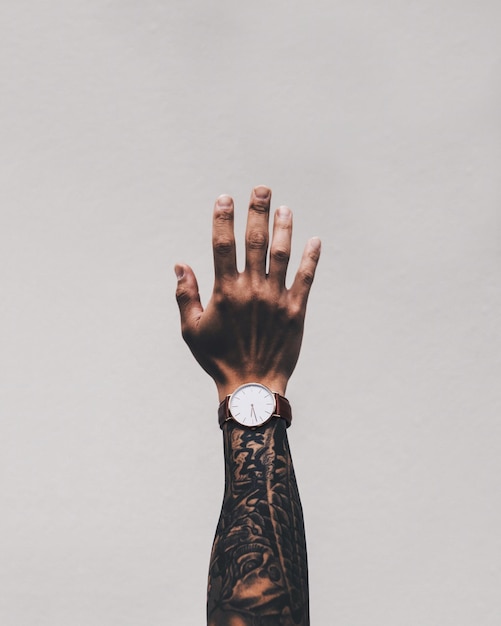 Image coupée d'une main d'homme tatouée portant une montre de poignet sur fond blanc
