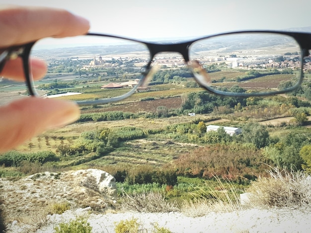 Photo image coupée d'une main tenant des lunettes contre le paysage