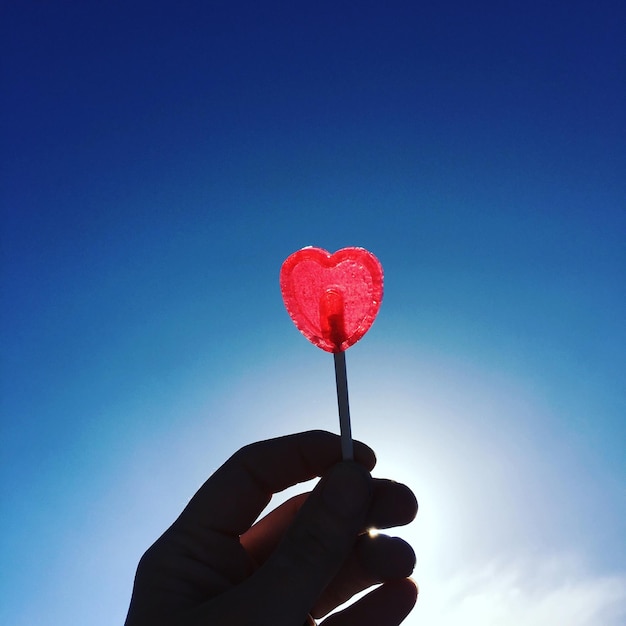 Image coupée d'une main tenant une sucette contre un ciel bleu clair