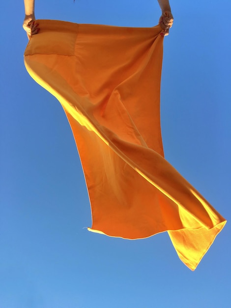 Image coupée de mains tenant du tissu contre un ciel bleu clair