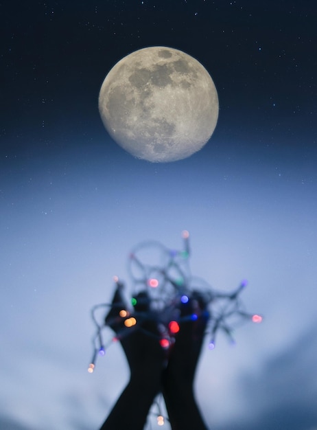 Image coupée de mains tenant un équipement d'éclairage éclairé avec la lune en arrière-plan