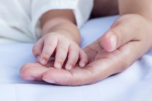 Image coupée d'un parent et d'un bébé se tenant par la main sur le lit à la maison