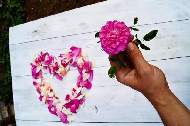 Image coupée d'une personne tenant une fleur contre une forme de cœur sur la table