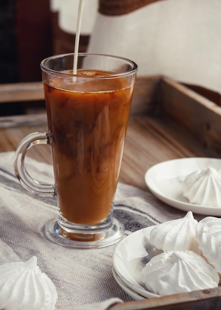 Image coupée d'un pot versant du lait dans une tasse par des meringues sur la table