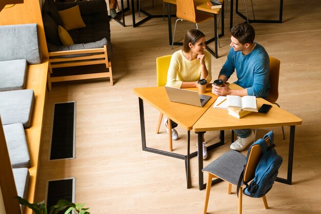 Image d'un couple d'amis jeunes étudiants dans la bibliothèque à faire leurs devoirs, lire et utiliser un ordinateur portable.