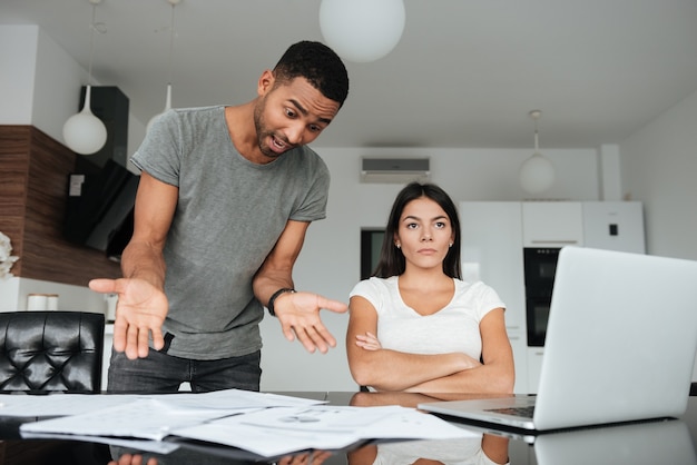 Image d'un couple d'amoureux discutant des factures domestiques à la maison. La femme regarde sérieusement de côté. Homme criant à la femme tout en tenant des documents.