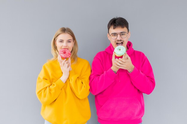 Image d'un couple heureux homme et femme souriant tout en mangeant des beignets sucrés ensemble