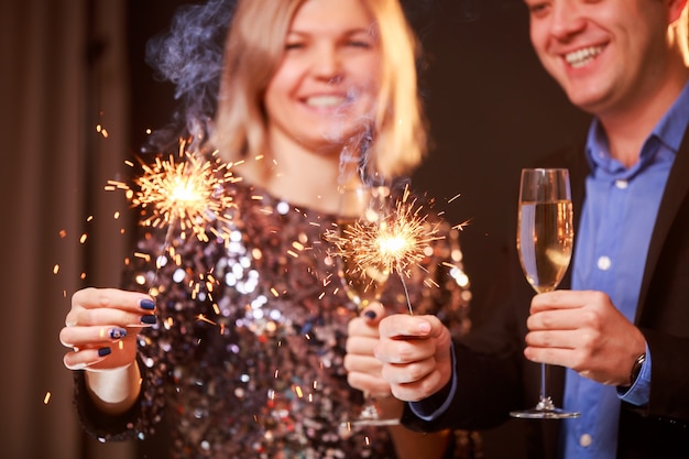 Image d'un couple heureux avec des verres de champagne et des cierges magiques sur fond noir