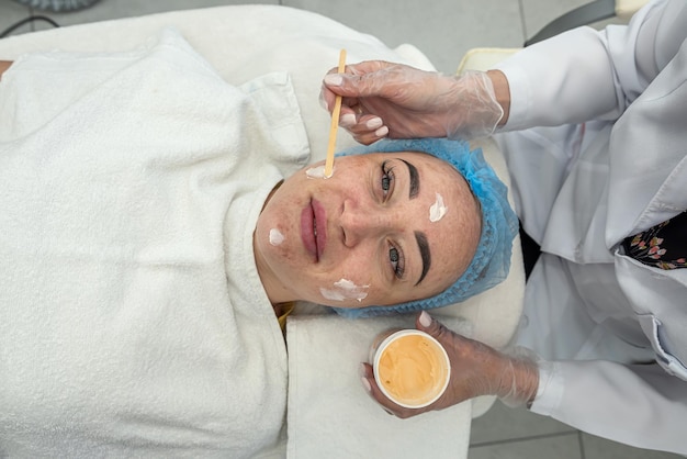 Image d'un dermatologue appliquant un masque à l'argile avec une brosse synthétique sur le visage d'un client