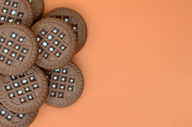 Image détaillée de biscuits sandwich ronds, brun foncé, fourrés à la noix de coco sur une surface orange.