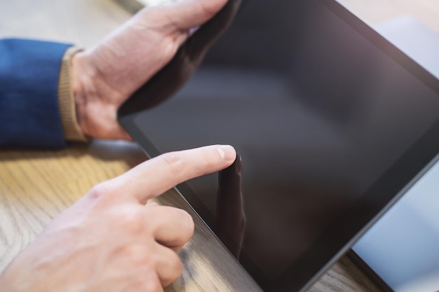 Image détaillée d'une main masculine interagissant avec une tablette numérique sur un bureau au milieu des environs vagues d'un environnement de bureau lumineux