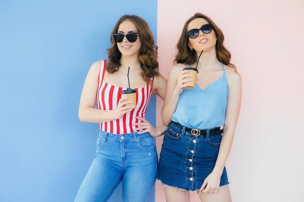 Image de deux femmes heureuses tenant du café à emporter dans des gobelets en papier isolés sur fond de couleur