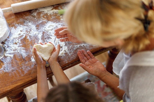 Image du cadre d'une femme et d'un enfant mains tenant la pâte en vue de dessus en forme de coeur. Ingrédients de cuisson sur la table en bois sombre. Vue horizontale.