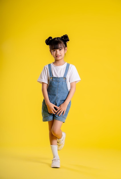 Image du corps entier d'une petite fille asiatique posant sur un fond jaune