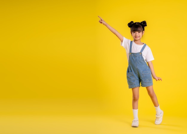 Image du corps entier d'une petite fille asiatique posant sur un fond jaune