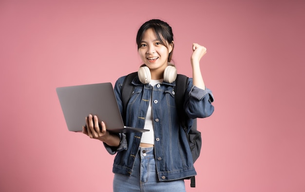 Image d'une étudiante asiatique tenant un ordinateur portable et isolée sur fond rose