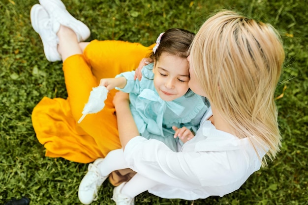 Image à l'extérieur d'une belle mère s'embrassant et se câlinant avec sa fille profitant du temps ensemble Jolie petite fille embrasse sa mère assise sur l'herbe verte dans le parc Fête des mères
