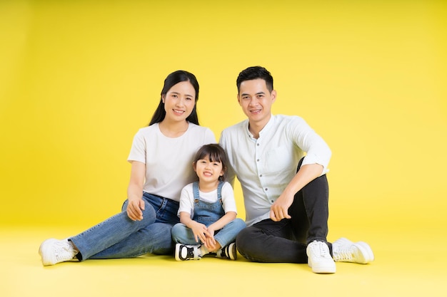 Image d'une famille asiatique assise ensemble heureuse et isolée sur fond jaune