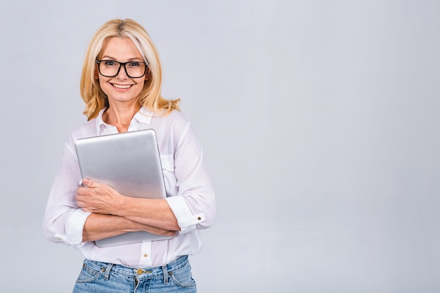 Image de femme d'affaires mature gaie debout isolé sur fond blanc à l'aide d'un ordinateur portable. Portrait d'une femme âgée souriante tenant un ordinateur portable.