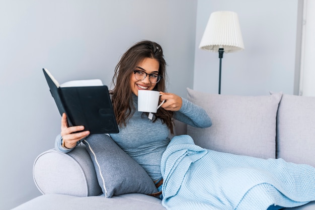 Image d&#39;une femme assise sur le canapé et lisant un livre à la maison