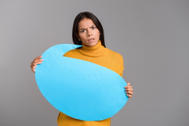 Image d'une femme confuse posant isolé sur mur gris mur tenant la bulle de dialogue.