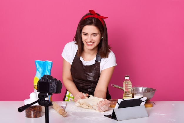 Image de femme heureuse, pétrir la pâte dans la cuisine devant un trépied avec appareil photo