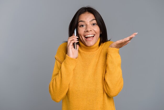 Image d'une femme heureuse posant isolé sur un mur gris parlant par téléphone mobile.