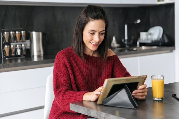 Image d'une femme incroyable à l'intérieur à la maison à la cuisine à l'aide d'un ordinateur tablette.