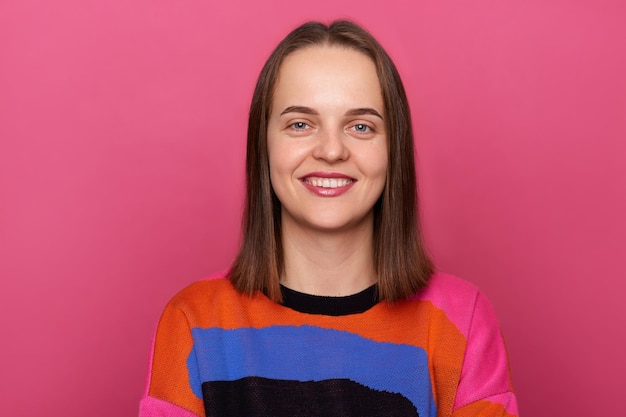 Image d'une femme joyeuse portant un pull posant contre un mur rose regardant la caméra avec un sourire à pleines dents étant de bonne humeur exprimant des émotions positives et du bonheur