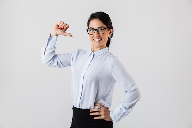 Image de femme secrétaire réussie portant des lunettes debout dans le bureau, isolé sur un mur blanc