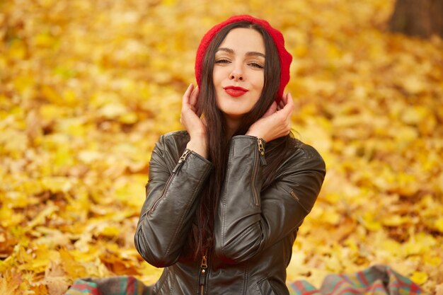 Image de femme séduisante, femme brune habille un béret élégant et une veste en cuir, regardant la caméra et souriant, posant en dehors, étant de bonne humeur