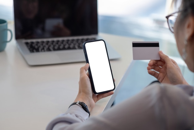 Image d'une femme tenant un smartphone et une carte de crédit au bureau. Concept de magasinage en ligne.