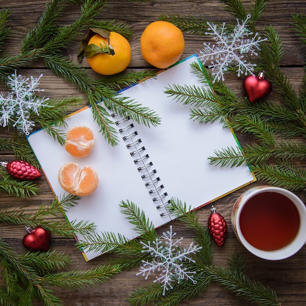 Image festive de nouvel an et Noël avec des branches de sapin, des flocons de neige, des mandarines, du thé, un bloc-notes ouvert