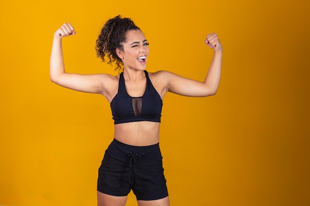 Image d'une fille afro-américaine forte et confiante, fléchissant les biceps et semblant sûre d'elle, debout sur fond jaune