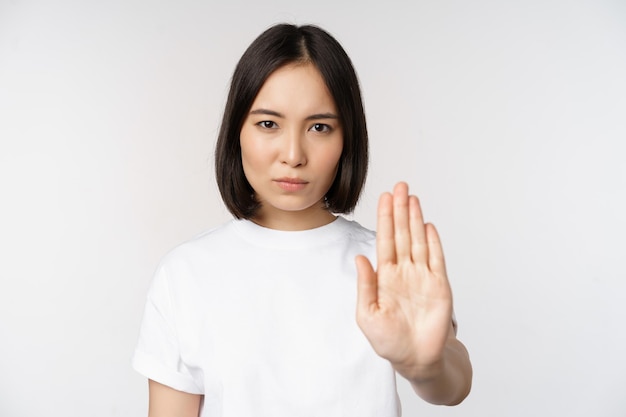 Image d'une fille asiatique montrant stop interdire qch étendre un bras pour montrer un geste tabou interdisant debout en t-shirt sur fond blanc