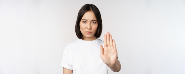 Image d'une fille asiatique montrant stop interdire qch étendre un bras pour montrer un geste tabou interdisant debout en t-shirt sur fond blanc