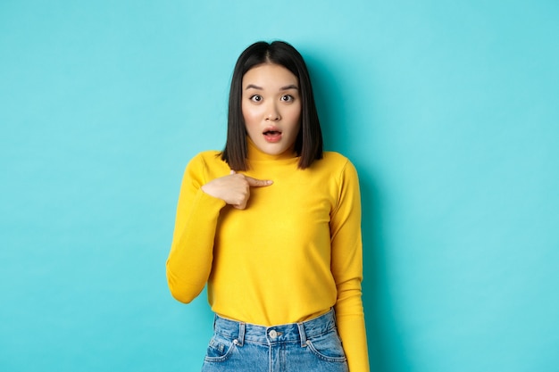 Image d'une fille asiatique surprise haletant et se montrant incrédule, debout sur le bleu.