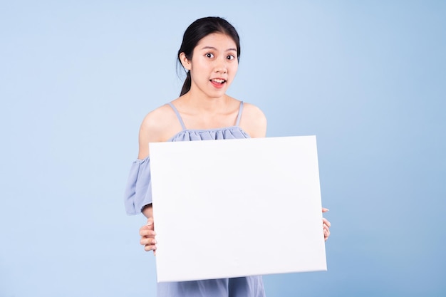 Image d'une fille asiatique tenant un tableau blanc, isolé sur fond bleu