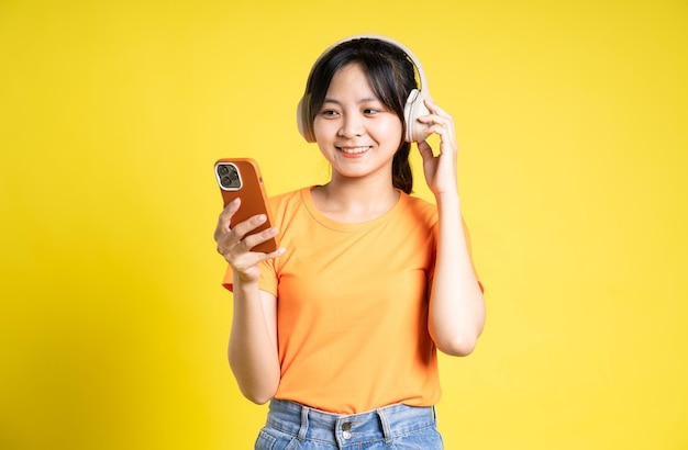 Image d'une fille asiatique utilisant un téléphone et isolée sur fond jaune