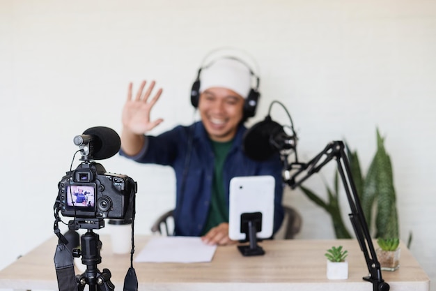 Image floue d'un homme asiatique faisant du contenu dans une salle de podcasting à l'aide d'une caméra professionnelle