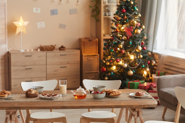 Image de fond de l'intérieur de la maison confortable avec arbre de Noël et table en bois avec des collations au premier plan, espace copie