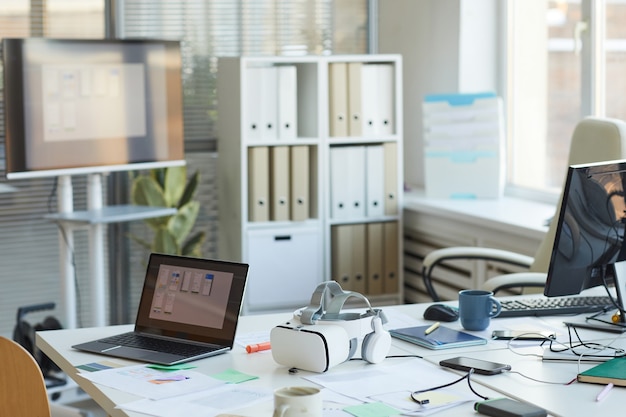 Image de fond de la salle de conférence en désordre dans le bureau des développeurs informatiques avec ordinateurs et casque VR sur table, espace de copie