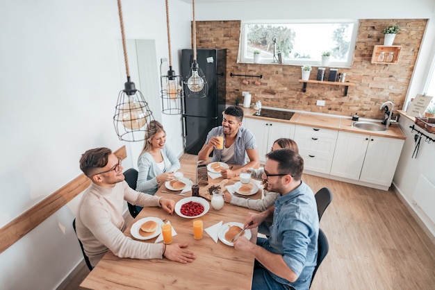 Image grand angle de cinq amis ou colocataires multiethniques en train de manger des pancakes faits maison.