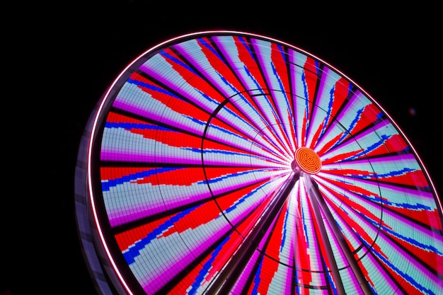 Image de la grande roue illuminée la nuit avec des rouges, des bleus, des gris et des violets