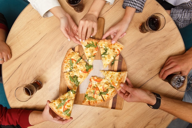 Image en gros plan d'amis partageant une pizza italienne traditionnelle et boire du thé dans un café