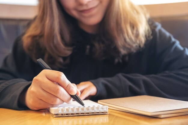 Image Gros plan d'une belle femme asiatique écrit sur un cahier vierge sur une table en bois