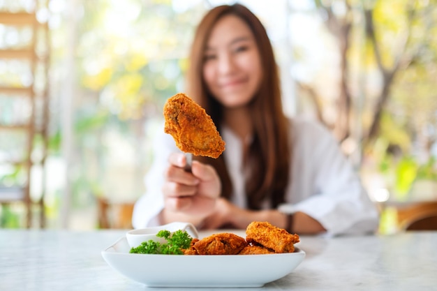 Image en gros plan d'une belle femme asiatique montrant et mangeant du poulet frit au restaurant