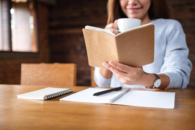 Image en gros plan d'une belle femme lisant un livre en buvant du café le matin